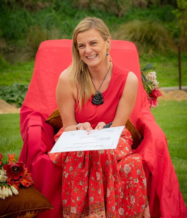 Lady outside dressed in red, in a red chair holding a certificate.